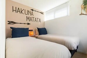 Ein Hotelzimmer mit zwei Betten, einem an der Wand befestigten Schild mit der Aufschrift 'HAKUNA MATATA' und einem Fenster mit Jalousien.