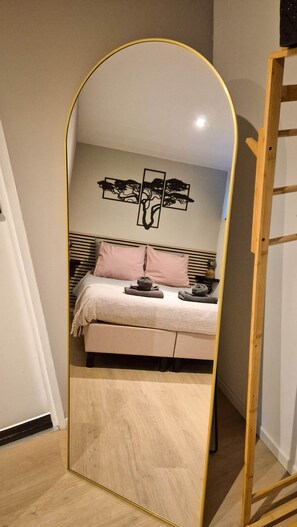 A bedroom with a bed, a headboard, a wall-mounted artwork, and a mirror with a wooden frame. - 't Bunga huiske (Bunga Holidays) (Lanaken)