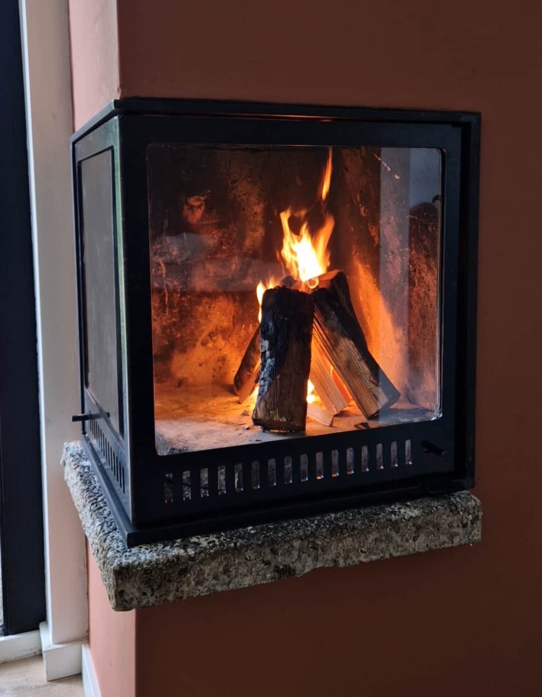 A fireplace with a stone base and a glass enclosure, displaying burning logs.