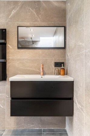 Un bagno moderno con uno specchio grande, un lavandino e un mobile contenitore nero sottostante.