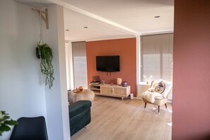 A living room with a flat-screen TV mounted on the wall, a wooden cabinet with decorative items, a green sofa, and a wicker chair. - 't Bunga huiske (Bunga Holidays) (Lanaken)