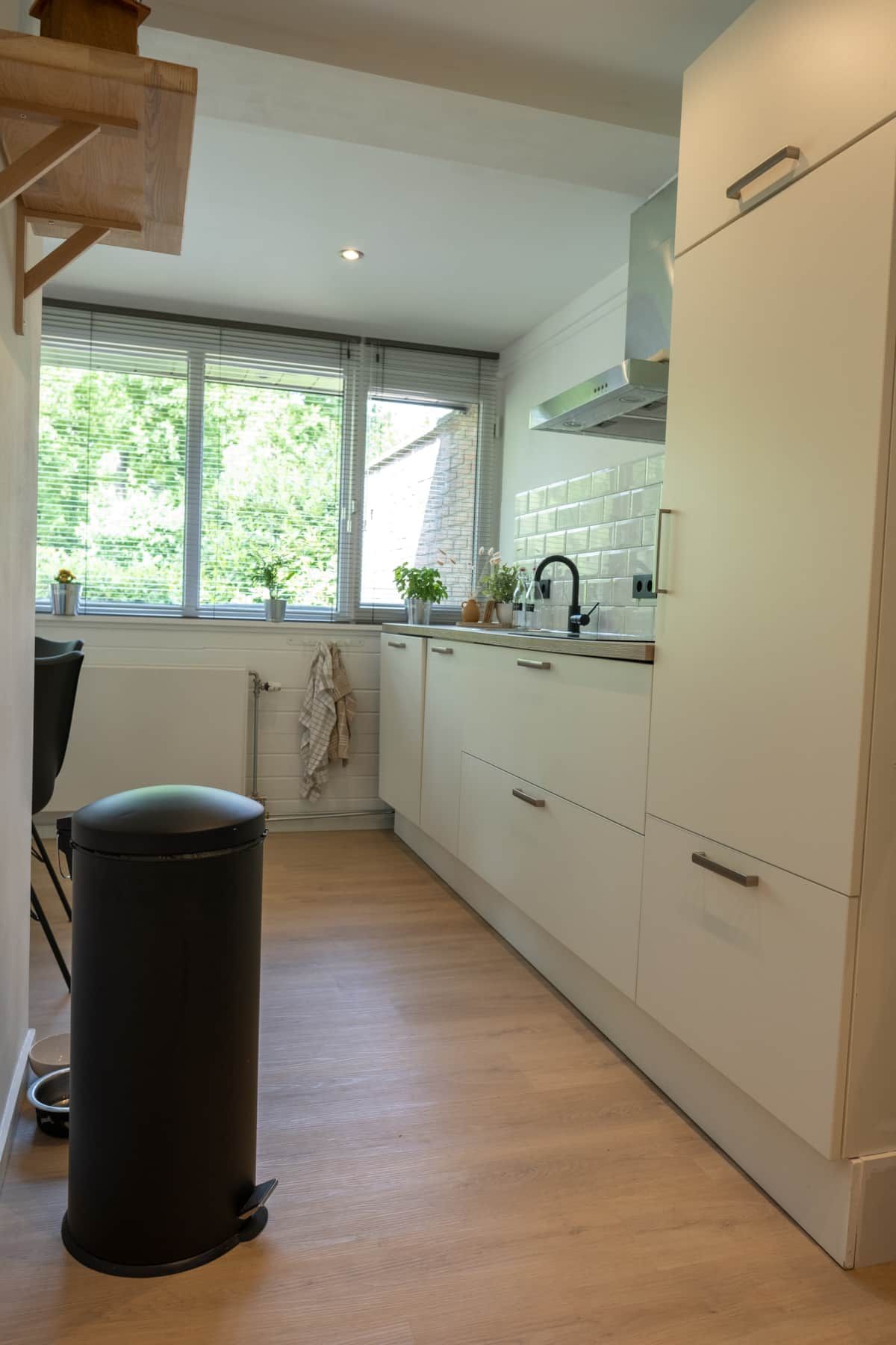 A modern kitchen with white cabinets, a black trash bin, and a window with a view of greenery.