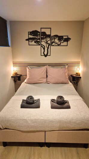 Un letto con due asciugamani, una testiera a listare orizzontali, lampade da comodino e un quadro appeso sopra il letto.