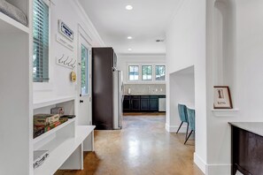 Eine moderne Küche mit einem Edelstahlkühlschrank, eine Essecke mit einem blauen Stuhl und ein Flur mit weißen Wänden und Holzboden.