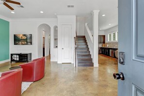 A spacious hallway with a staircase leading to a kitchen area, a dining area with red chairs, and a painting on the wall. - Spacious 4 BDRM I Central Austin I Sleeps 14 (Austin)
