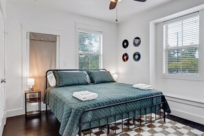 Ein Schlafzimmer mit Bett, Nachttisch, Lampe, an der Wand befestigten Schallplatten und einem Fenster mit Jalousien.