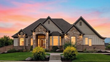 A two-story house with a stone facade, a front entrance with a door, and a landscaped front yard with shrubs and a pathway.