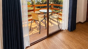 Una habitación con una puerta corrediza de vidrio que da a un espacio exterior con terraza de madera, dos sillas de mimbre y una pequeña mesa redonda.