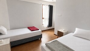 Ein Hotelzimmer mit zwei Betten, einem kleinen Nachttisch, einer Lampe und einem Fenster mit Vorhängen sowie einer Deckenleuchte.