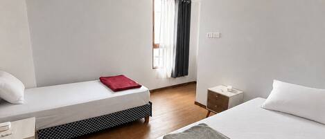A hotel room with a bed, a smaller bed, a nightstand, a desk, and a window with curtains.