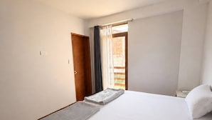Una habitación de hotel con una cama grande, una puerta de madera y un ventanal con cortinas.