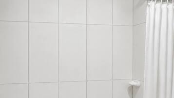 A shower area with white tiles, a showerhead, and a white curtain.