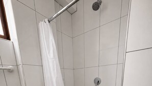 Un espacio de ducha con cortina blanca, un cabezal de ducha de mano y un grifo instalado en la pared.