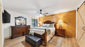 A bedroom with a wooden headboard, a bed with pillows, a nightstand with a lamp, a dresser, and a ceiling fan. - Gold Bear by Avantstay Hot Tub + Big-screen Movie Room + Grill Deck Near Lifts + Village (Truckee)