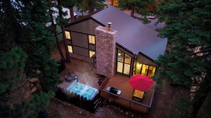 A two-story house with a stone chimney, a hot tub, and a deck with outdoor furniture. - Gold Bear by Avantstay Hot Tub + Big-screen Movie Room + Grill Deck Near Lifts + Village (Truckee)