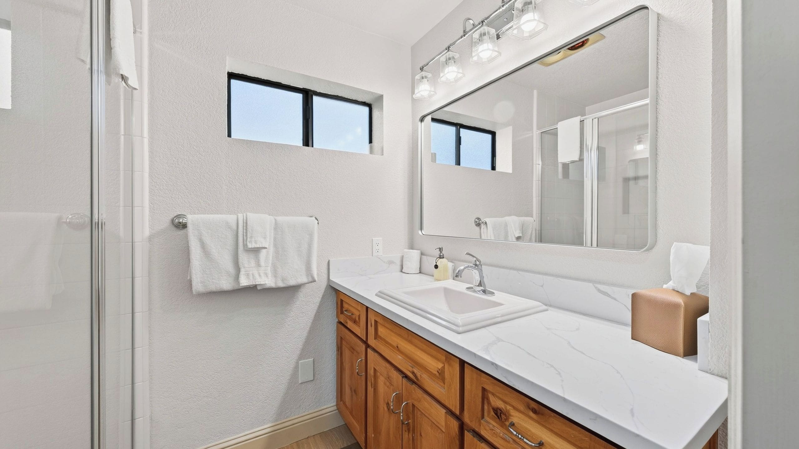 A modern bathroom with a glass shower enclosure, a large mirror with lights, and wooden cabinets.