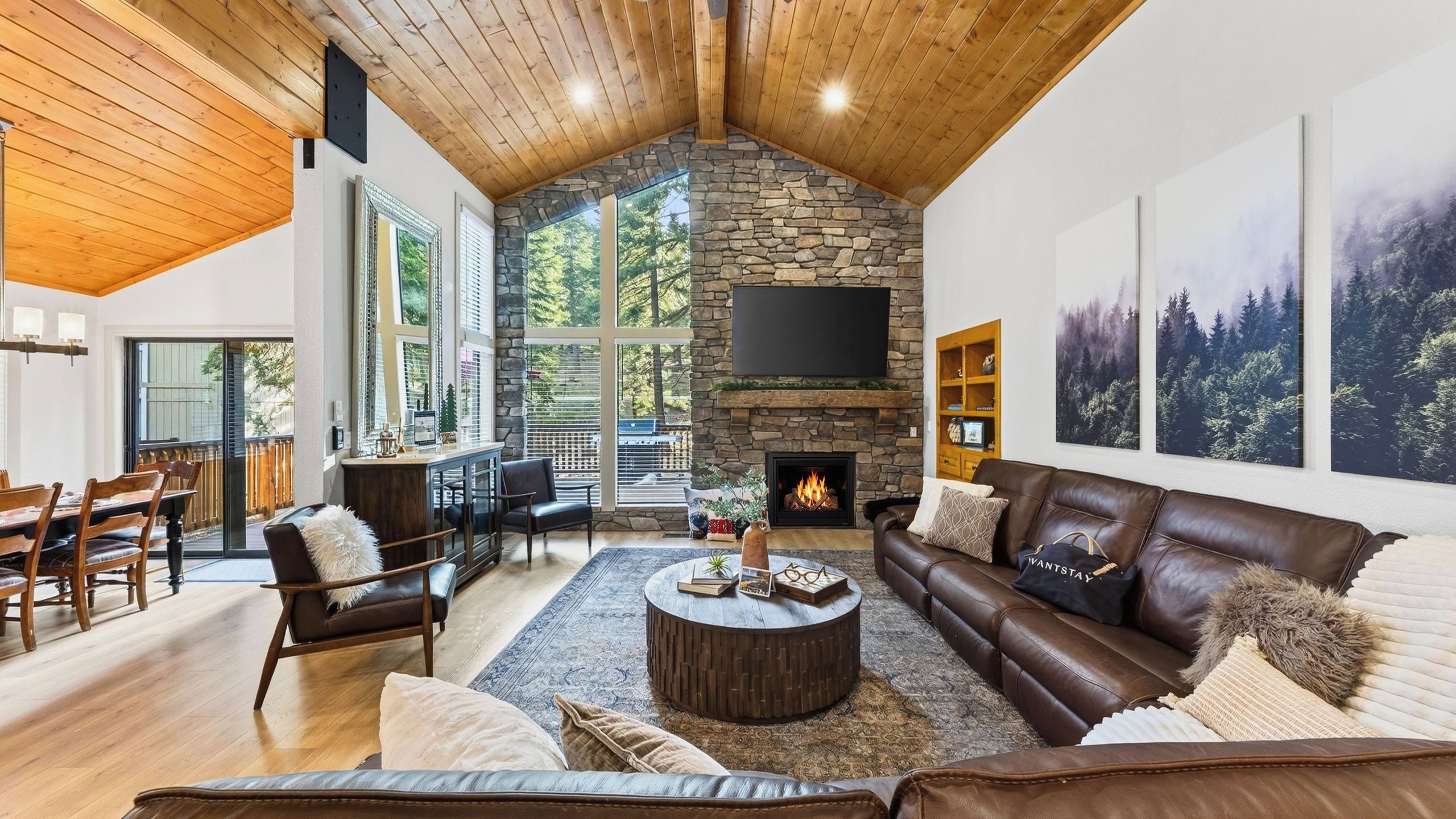 A spacious living room with a stone fireplace, leather sofa, and a large TV mounted on the wall.