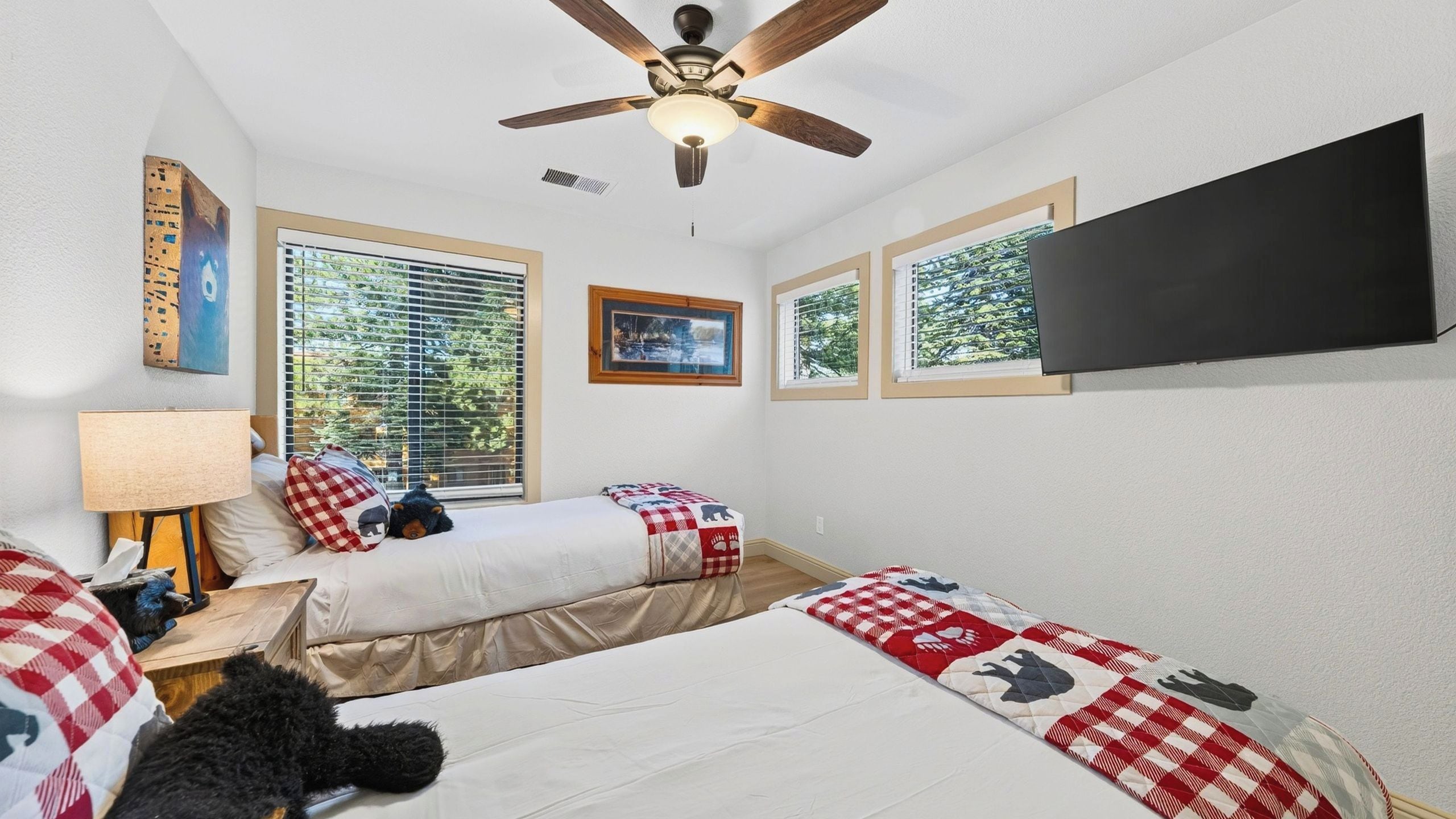 A bedroom with two beds, a ceiling fan, a TV, and windows with blinds.