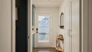 A hallway with a wooden floor, a door leading outside, and a small table with a kettle and a mirror.