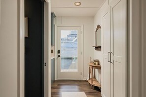 Un corridoio con pavimento in legno, una porta che dà all'esterno e un tavolino con bollitore e specchio.