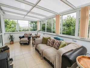 A conservatory with a sofa, armchair, and a small table with a lamp. - Llain (Cardigan)