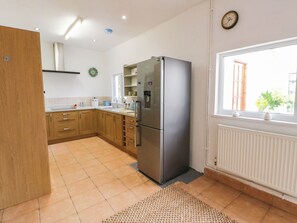 A kitchen with wooden cabinets, a stainless steel refrigerator, a window with a view, and a clock on the wall. - Llain (Cardigan)
