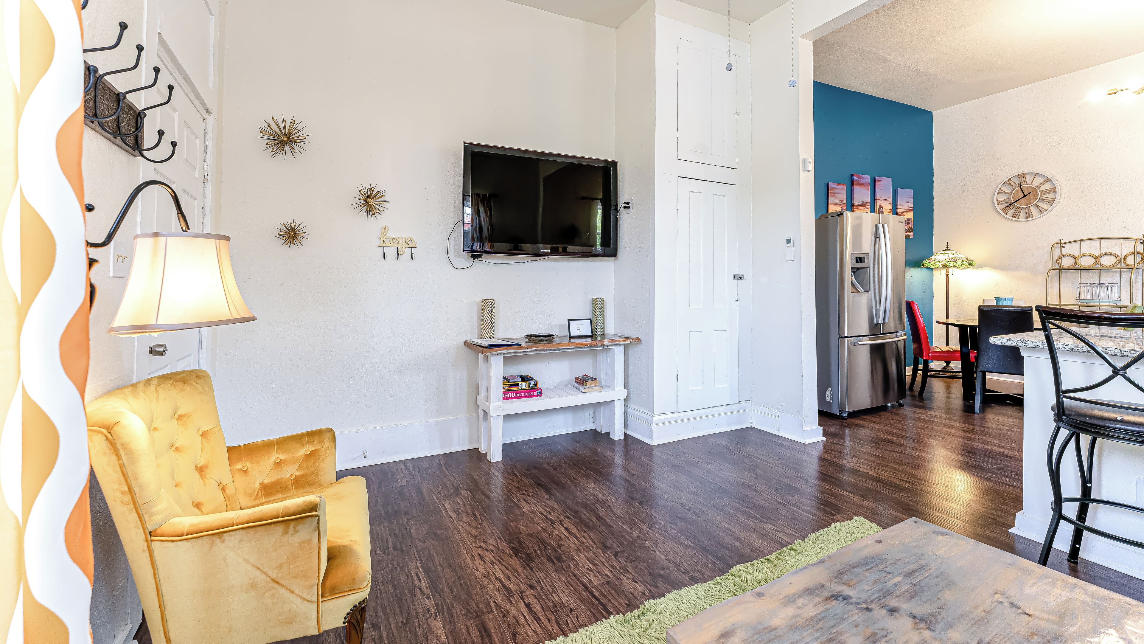 A living room with a television, a sofa, a dining table with chairs, and a kitchen area with a refrigerator.