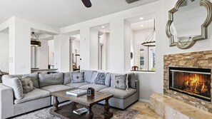 A modern living room with a sectional sofa, a fireplace, and a dining area visible through an open doorway.