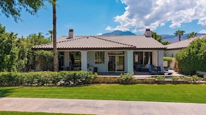 A two-story house with a tiled roof, a covered patio with outdoor seating, and a well-maintained lawn.
