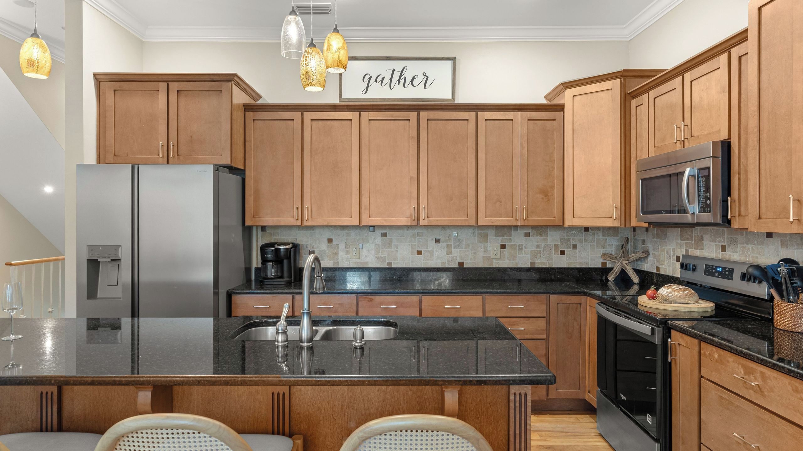 A modern kitchen with wooden cabinets, a stainless steel refrigerator, a microwave, and a large island with a sink.