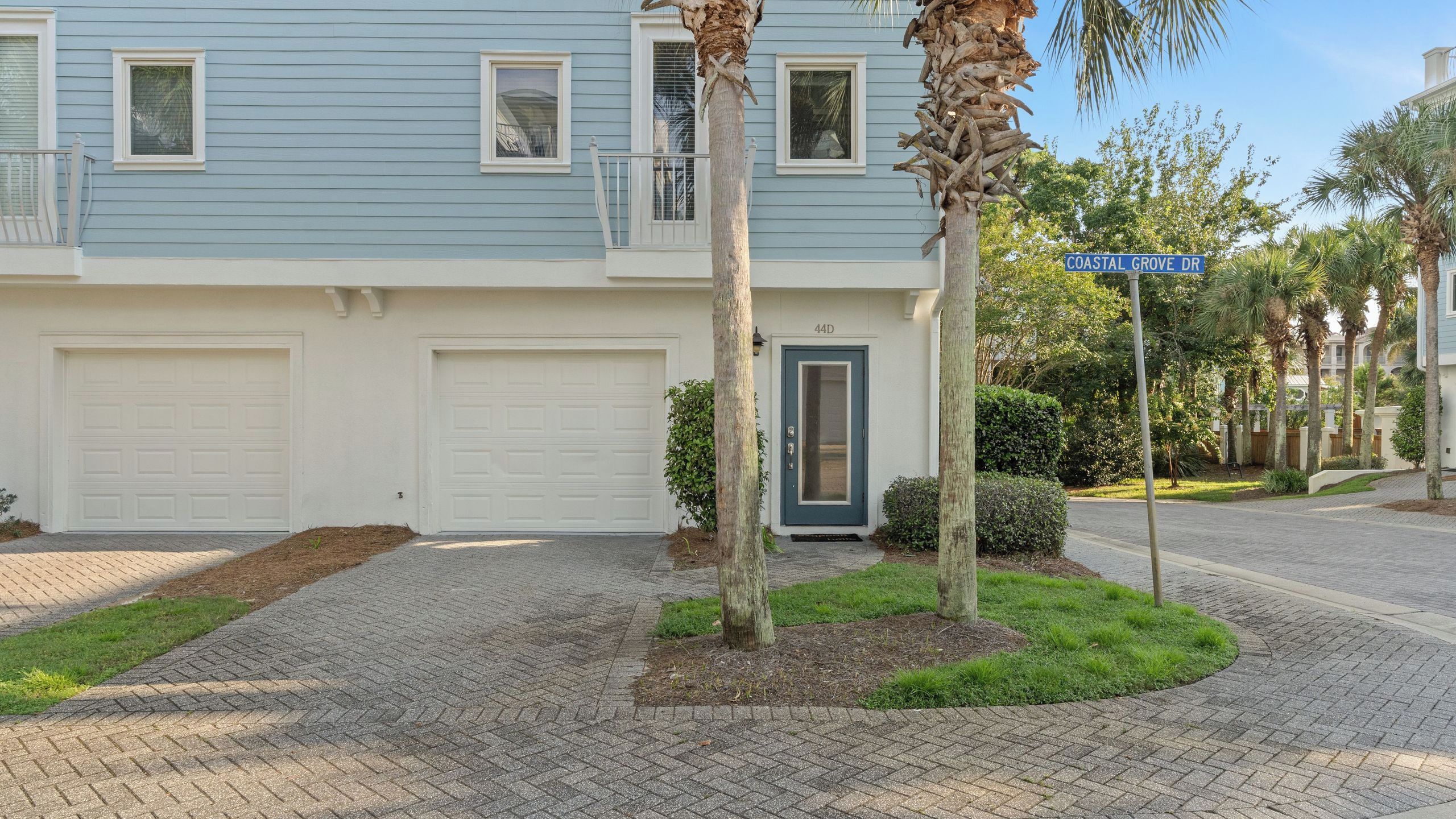 A residential building with a blue facade, two garage doors, a front door, and a street sign indicating 'COASTAL GROVE DR'.