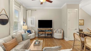 A living room with a sofa, a coffee table, a TV, and a dining area with a chair and table. - Drift & Dwell 30A by Avantstay Rooftop Terrace + Pool Access Walk to Beach + Gulf Place (Santa Rosa Beach)