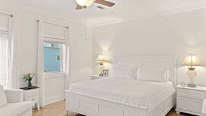 Quarto branco com cama, duas mesas de cabeceira com abajures, uma janela e uma porta.