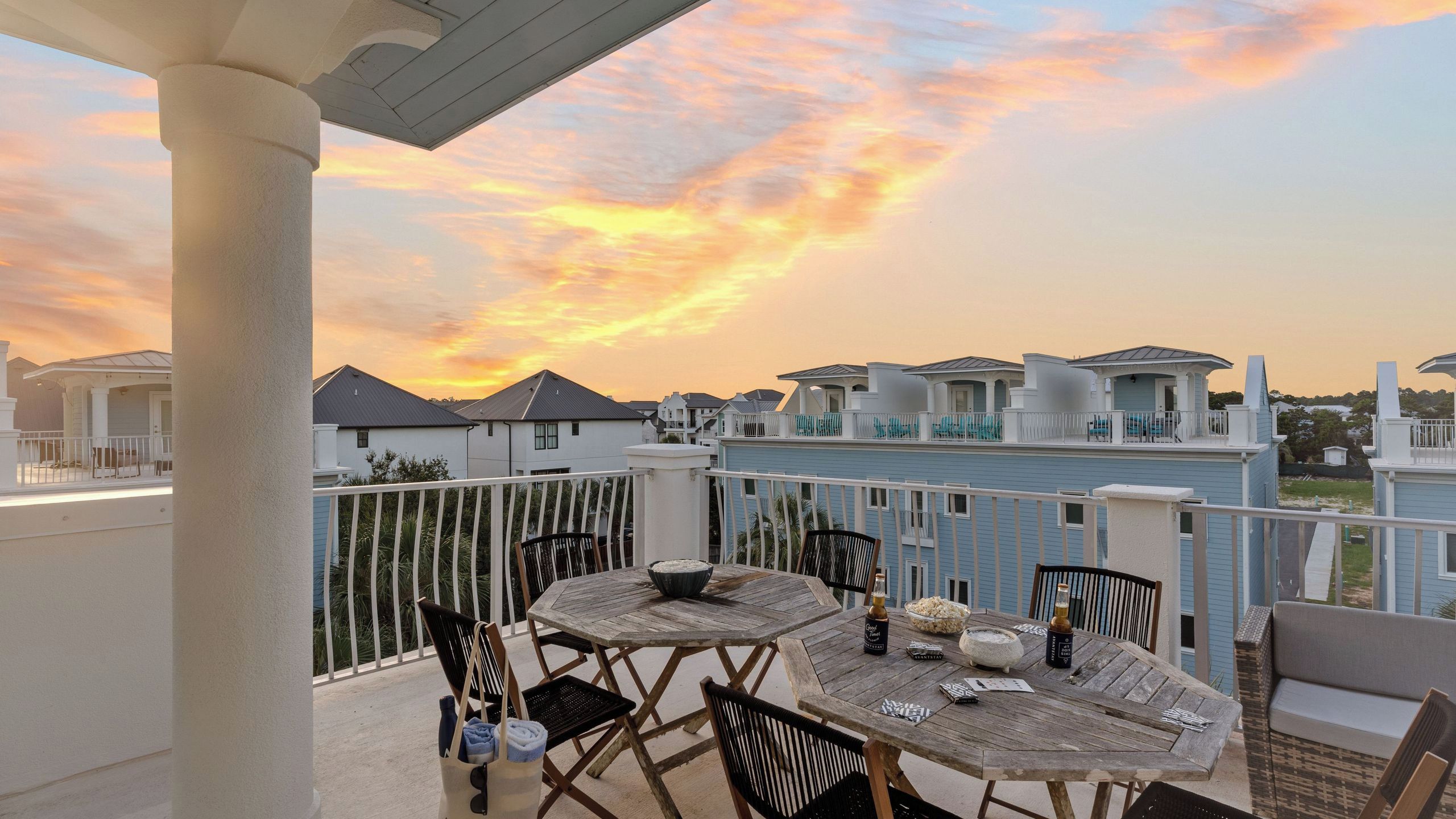 A balcony with a wooden table and chairs, a bottle of beer, and a bowl of popcorn.