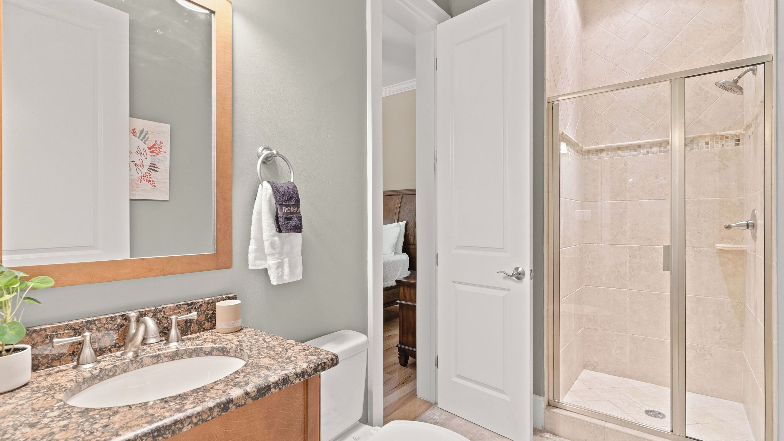 A bathroom with a granite countertop, a white sink, a mirror, and a shower with a glass door.