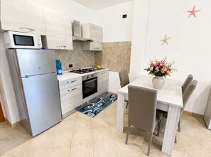 A compact kitchen with a refrigerator, stove, microwave, and oven. There is a dining table with chairs and a vase with flowers. - Hot tub and terrace surrounded by greenery – Sea & Soul Sardinia (Valledoria)