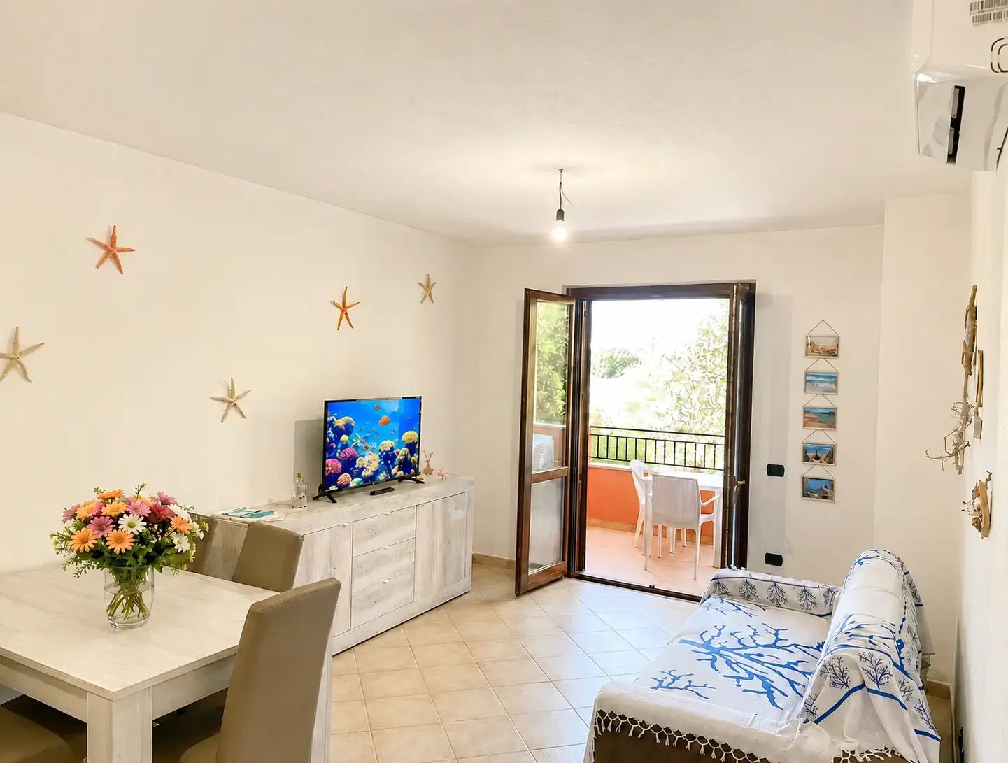 A room with a dining table, a TV on a cabinet, a sofa, and a balcony with outdoor furniture.
