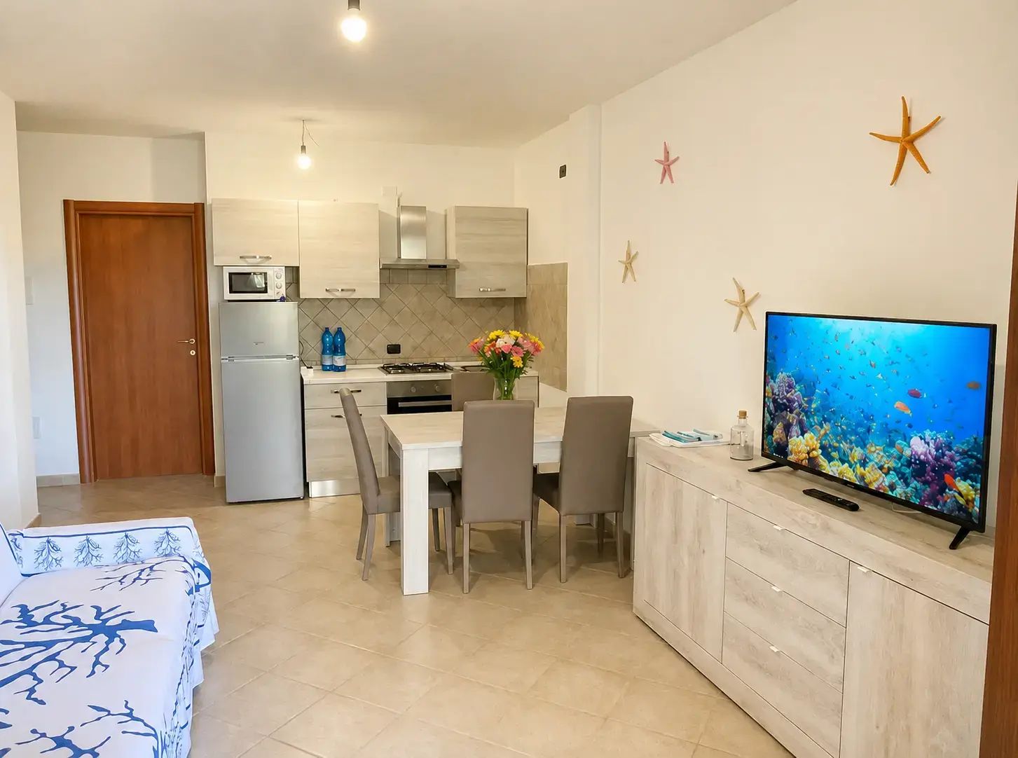 A modern kitchen with a dining area, a TV, and a decorative starfish wall.