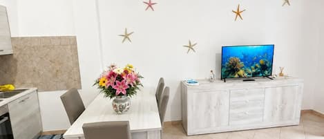 A modern living room with a dining table, chairs, a TV, and decorative starfish on the wall.
