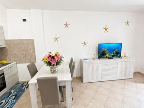 A modern living room with a dining table, chairs, a TV, and decorative starfish on the wall. - Hot tub and terrace surrounded by greenery – Sea & Soul Sardinia (Valledoria)