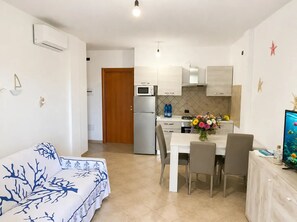 A modern kitchen with a refrigerator, microwave, and a dining table with chairs. - Hot tub and terrace surrounded by greenery – Sea & Soul Sardinia (Valledoria)