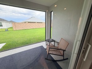 Ein Zimmer mit Glastür, die auf einen Balkon führt, einem kleinen Tisch und einem Korbsessel.