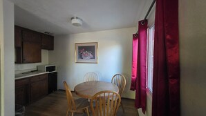Cozinha compacta com armários de madeira, micro-ondas e área de refeições com mesa e cadeiras de madeira.