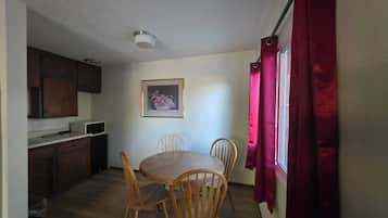 A compact kitchen with wooden cabinets, a microwave, and a dining area with a wooden table and chairs.
