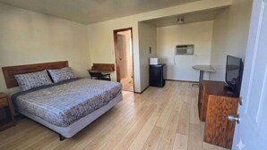 Quarto com cama, escrivaninha, televisão e ar condicionado.
