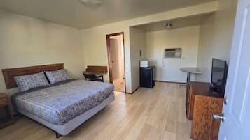 A bedroom with a bed, a desk, a television, and an air conditioning unit.