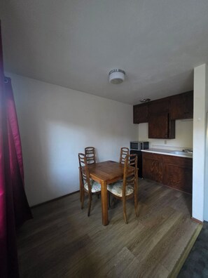 A compact kitchen with wooden cabinets, a microwave, and a dining table with four chairs.