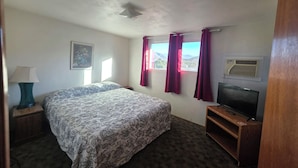 Quarto com cama, televisão, janela com cortinas e um quadro na parede.