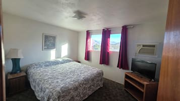 A bedroom with a bed, a television, a window with curtains, and a painting on the wall.
