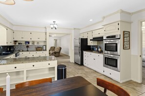 Una cocina moderna con armarios blancos, encimeras de granito, electrodomésticos de acero inoxidable y un comedor con mesa y sillas de madera.
